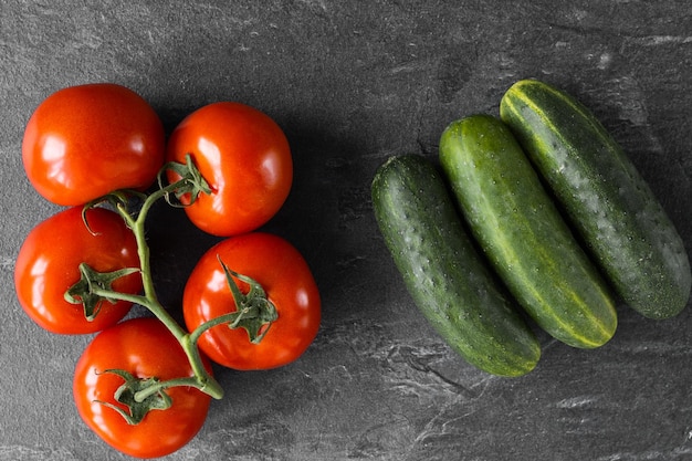 Three cucumbers and tomato on dark background