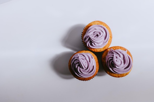 Three cupcakes with purple icing top view white background and shadows