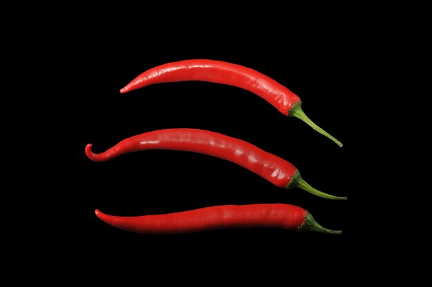 Three cute red hot chili pepper on black surface