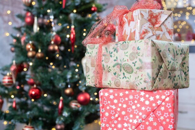 Three decorated present boxes in craft paper with bows for New year and Christmas holiday and fir tree with toys ball on branches at background