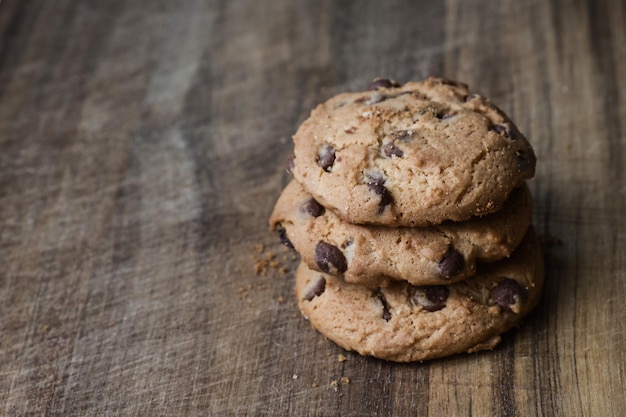 Three delicious biscuits with chocolate pieces in stack on wooden table