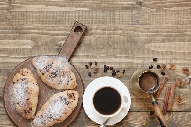 Three delicious freshly baked croissants and cup of coffee on wooden board. Top view. Breakfast. Copy space.