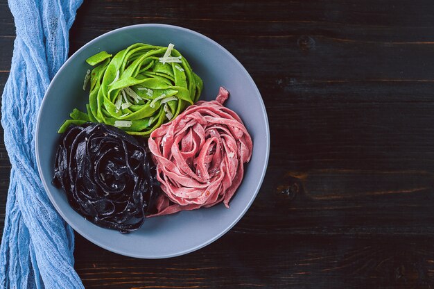 세 가지 맛있는 파스타. 검은 페이스트, 녹색 파스타 및 파스타 자홍색. 나무 테이블에 회색 접시입니다.