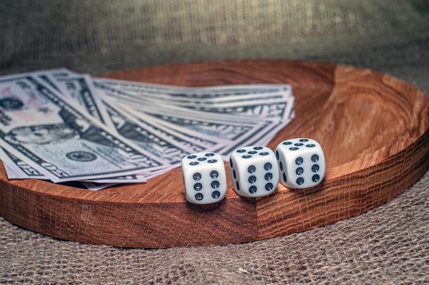 Three dice laying over a pile of money on a wooden plate