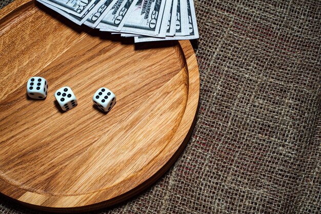 Three dice laying over a pile of money on a wooden plate