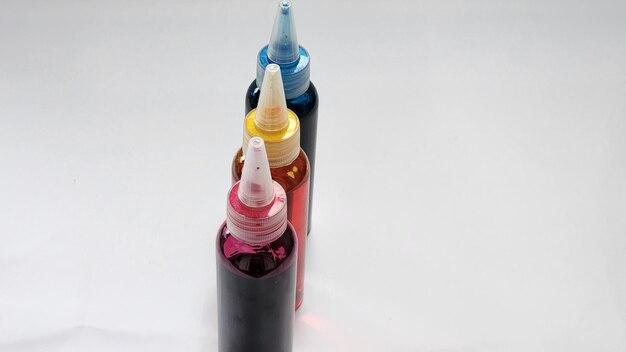 Фото Три разных цветных бутылки чернил выставлены на белой поверхности
