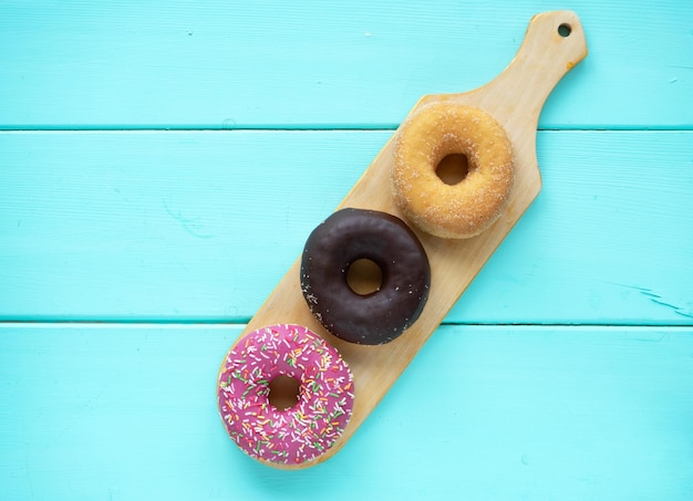 사진 세 가지 다른 도넛 초콜릿 도넛 핑크 장식과 나무 파란색 배경에 나무 커팅 보드에 장식 없이