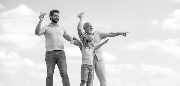 Three different generations ages grandfather father and child son playing with toy plane outdoors