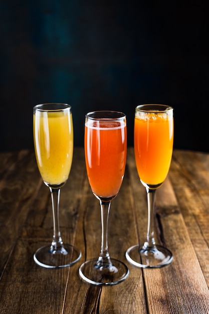 Three different sparkling fruity cocktails, red, yellow and orange, in flute glasses