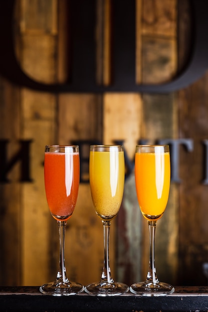 Three different sparkling fruity cocktails, red, yellow and orange, in flute glasses