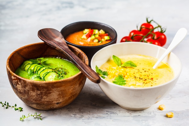 Three different vegetable cream soups in bowls on gray  Corn, cucumber and gazpacho soups,