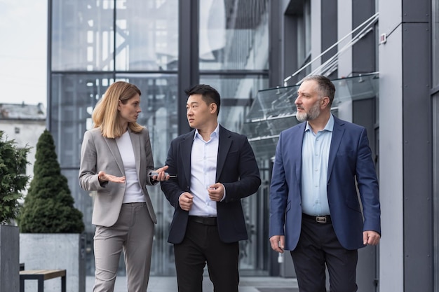 Three diverse business people walking and talking focused and thoughtful seriously outside office