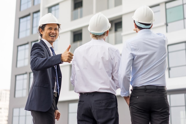  three diverse business people wearing helmets and standing outdoors 