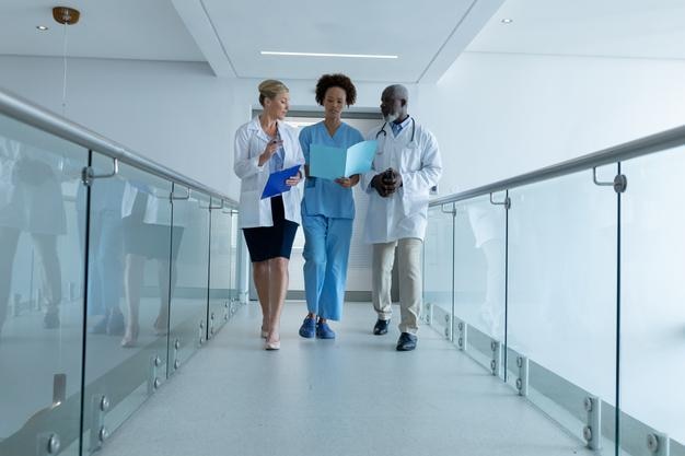 Photo three diverse male and female doctors walking through hospital corridor looking at document