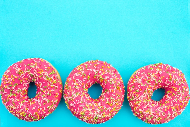 Three donuts with bright pink icing on blue turquoise background