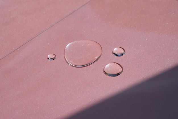 Three drops of cosmetics or perfume on a pink background