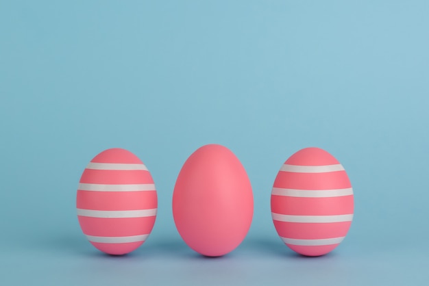 Three Easter decorated pink eggs. Striped pink eggs in a row on a blue background. White strips. Copy space. Pink monochrome Easter concept.