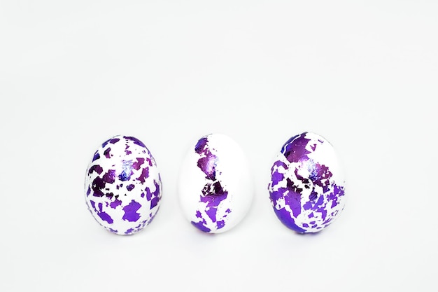 Three Easter eggs with pieces of decorated foil in a row on a white background