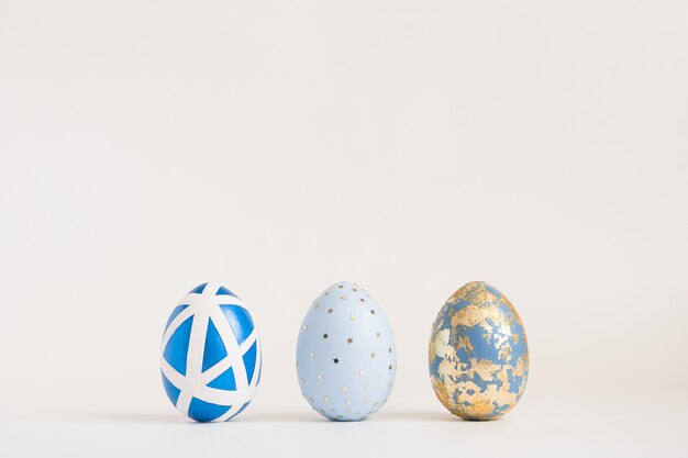 Three Easter golden decorated eggs on blue surface. Minimal easter concept. 