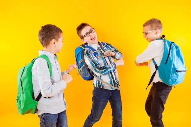 Three elementary school boys having fun on a yellow background the schoolboys wear clothes casual style with backpacks