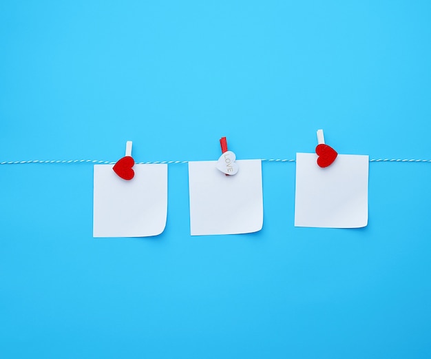 Three empty square white paper sheets hanging on decorative clothespins