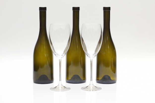 Three empty upturned wine bottles and two glasses on a white
