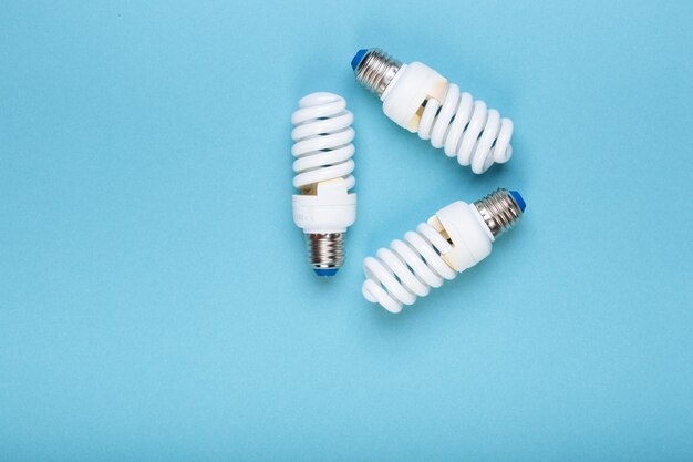 Three Energy saving lamps in the shape of a recycling symbol Eco green energy concept Isolated on the blue caption for text