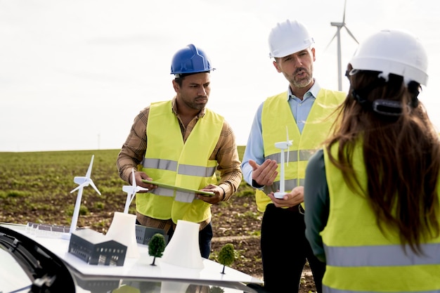 Photo three engineers standing on wind turbine field and discussing lively over plastic models