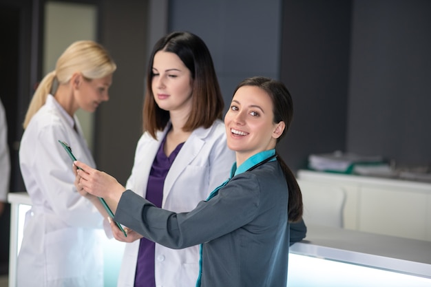 Три женщины-врача разговаривают возле стойки регистрации в неврологической клинике