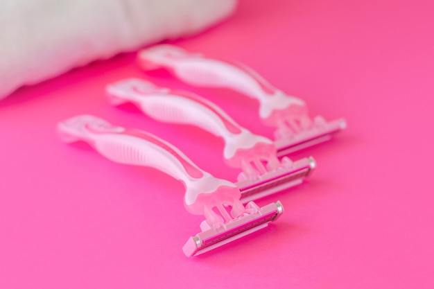 Three female pink razor with a white towel on pink. Spa and female treatments, epilation