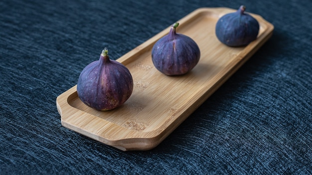 Three figs on a wooden tray on a black background closeup