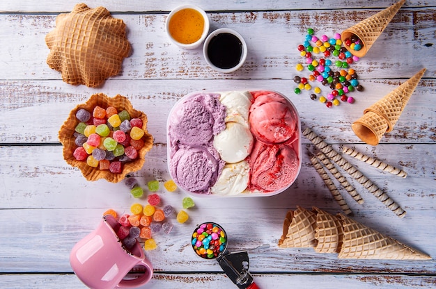 Three flavors of ice cream in a delivery container, making a composition with several cones and colored gums. Top view