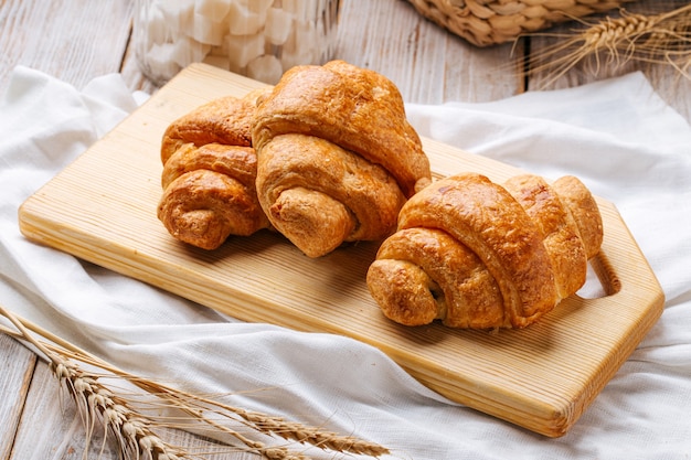 Three french croissants on the wooden cutting board decorated with wheat and napkin