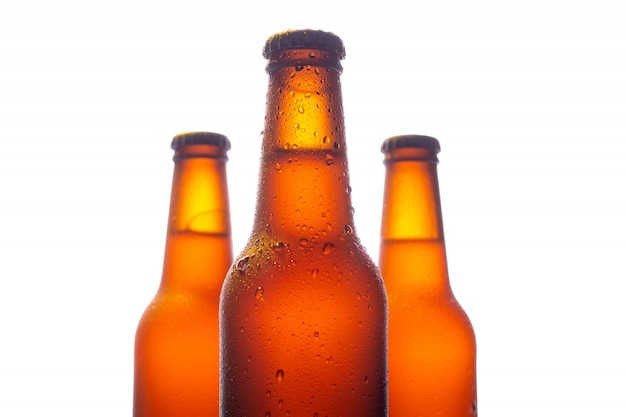 Three fresh beer bottle with big water drops on white wall