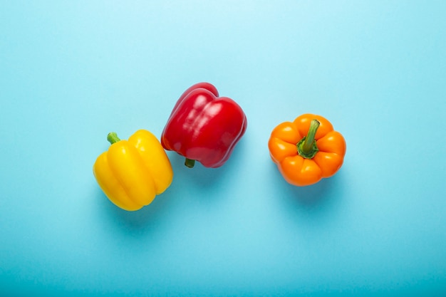 Three fresh bright sweet peppers on a blue background. Top view, flat lay.