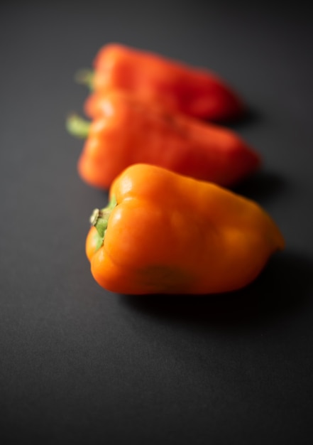 three fresh orange bell peppers on a dark background