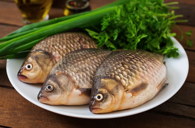 Three fresh raw crucian on a wooden background with herbs