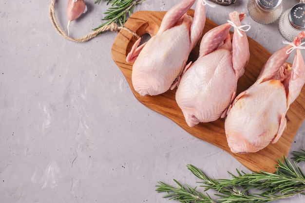 Three fresh raw organic quails on wooden board on a gray background, Top view, Space for text