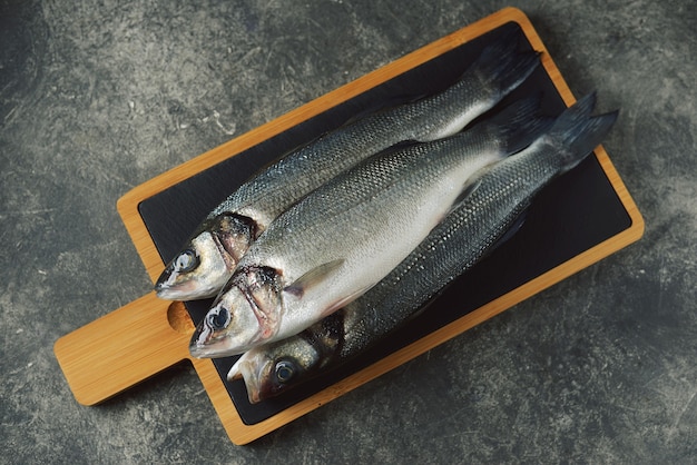 Three fresh raw sea bass on a serving board