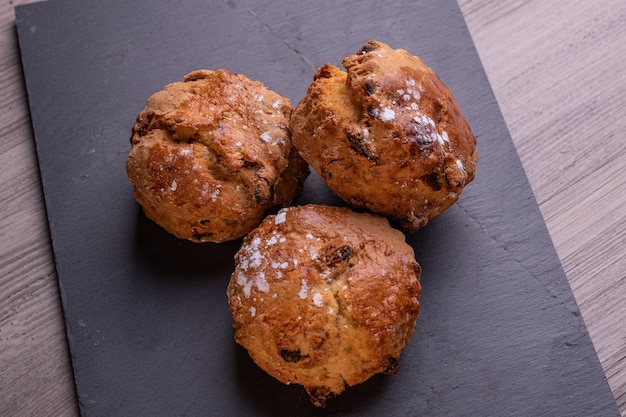 Three freshly baked fruit scones on slate plate .Rustic surface.