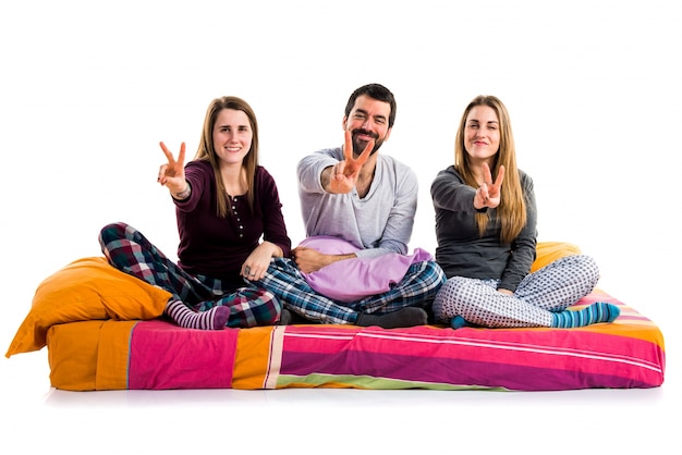 Three friends on a bed doing victory gesture