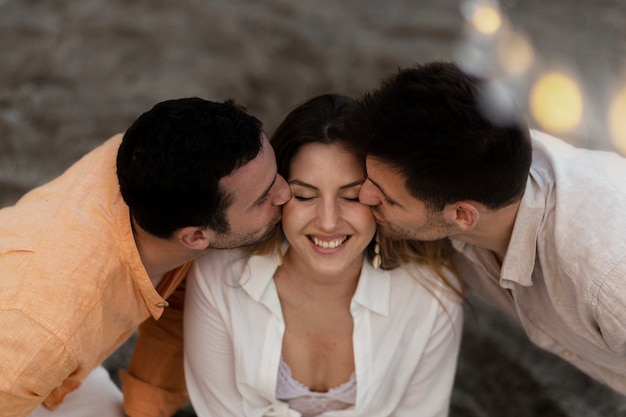 Three friends kissing while posing together during a beach party