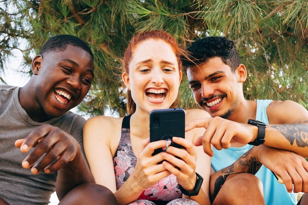 Photo three friends look at the smartphone after exercising outdoors