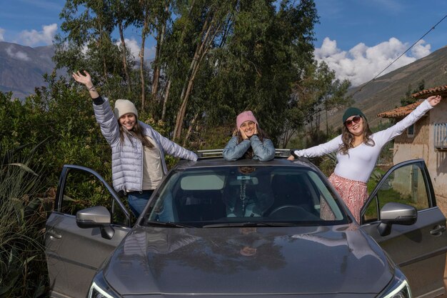 Three friends standing out of a car with their arms raised in the mountains