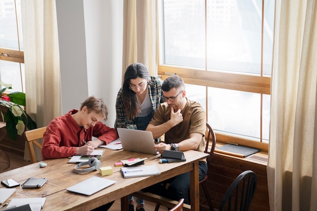 Three friends using a laptop and a notebook to learn during study session