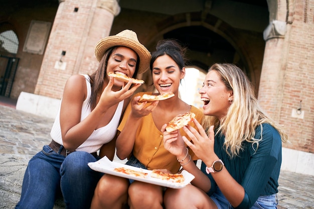 3人の面白い多人種の女性が外でピザを食べて 幸せな女性友達が楽しんでいます