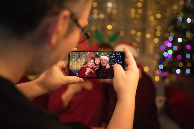 Riunione di famiglia da tre generazioni per le vacanze di natale. figlio che prende l'immagine del nipote sorridente caucasico che abbraccia i suoi nonni con il telefono cellulare. insieme e concetto di valori familiari.