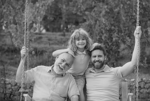 Three generations of men together portrait of smiling son father and grandfather swinging on the swi
