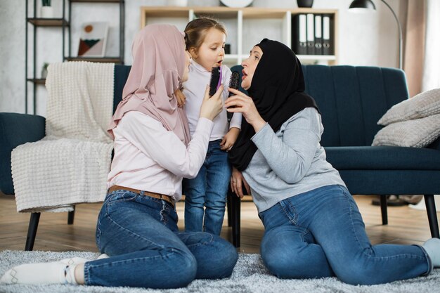 リビング ルームのソファの近くの床に膝の上に座っている 3 世代のイスラム教徒の女性