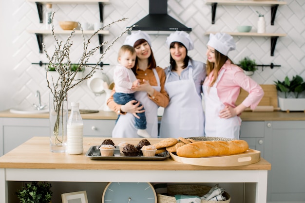 Three generations of women are cooking in the kitchen, focus on the table with maffines and cookies. Homemade food and little helper. Happy family. Baking in kitchen. Easter holidays or mothers day